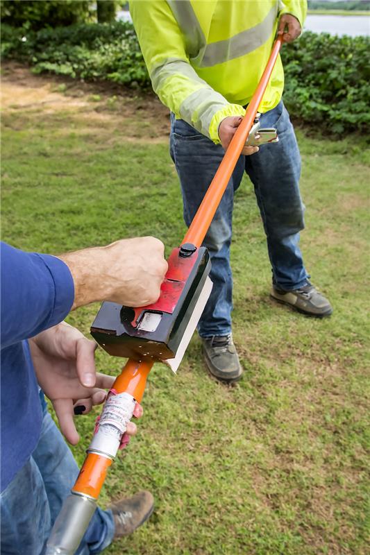 Foam cored insulated hot stick being used for field inspection by two workers in safety gear outdoors.