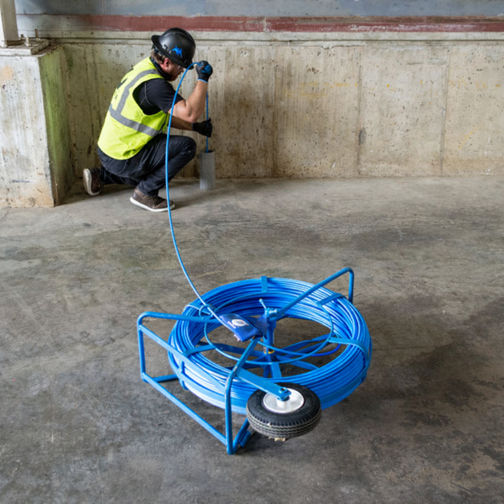 Worker feeding a Condux Python duct rodder into conduit at an industrial jobsite